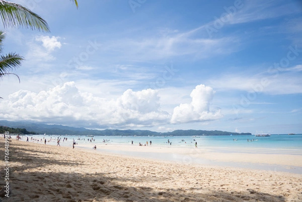 Fototapeta Sunny tropical beach with people swimming and relaxing by turquoise sea and white clouds over distant hills