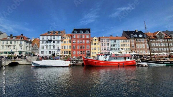 Fototapeta 07 August, 2024, Copenhagen city center, Denmark Summer day scenic canal with boats and tourists, cyclists riding along colorful buildings and waterfront, vibrant urban atmosphere in European capital