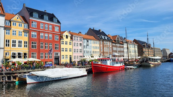 Fototapeta 07 August, 2024, Copenhagen city center, Denmark Summer day scenic canal with boats and tourists, cyclists riding along colorful buildings and waterfront, vibrant urban atmosphere in European capital