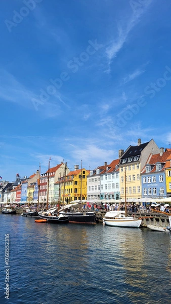 Fototapeta 07 August, 2024, Copenhagen city center, Denmark Summer day scenic canal with boats and tourists, cyclists riding along colorful buildings and waterfront, vibrant urban atmosphere in European capital
