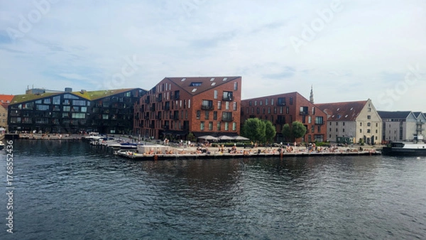 Fototapeta 07 August, 2024, Copenhagen city center, Denmark Summer day scenic canal with boats and tourists, cyclists riding along colorful buildings and waterfront, vibrant urban atmosphere in European capital