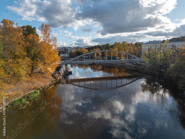 Obraz A river landscape with colorful autumn trees and an arched bridge mirrored in calm water.