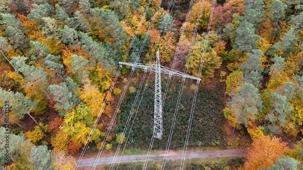Fototapeta High voltage power lines through colorful autumn forest – aerial view