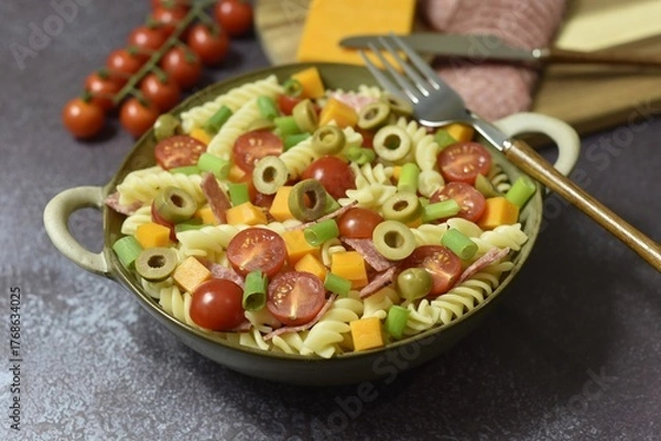 Fototapeta Durum wheat semolina pasta salad made with peppered salami cherry vine tomatoes red leicester cheese green pitted olives and spring onions.