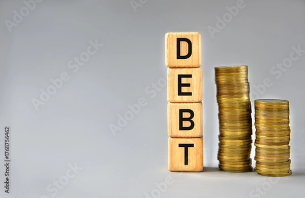 Fototapeta DEBT - word on wooden cubes on the background of stacks of coins