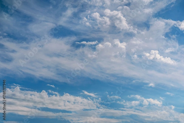 Fototapeta Wide view of blue sky with soft white clouds drifting gently across the frame. Concept of freedom, open space, peaceful atmosphere. Natural background
