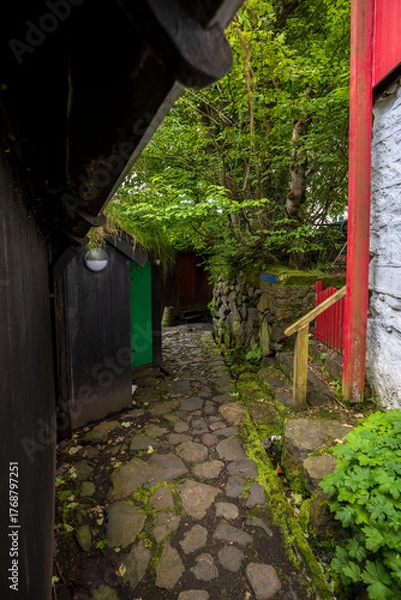 Obraz Narrow cobblestone alley with colorful wooden walls and greenery