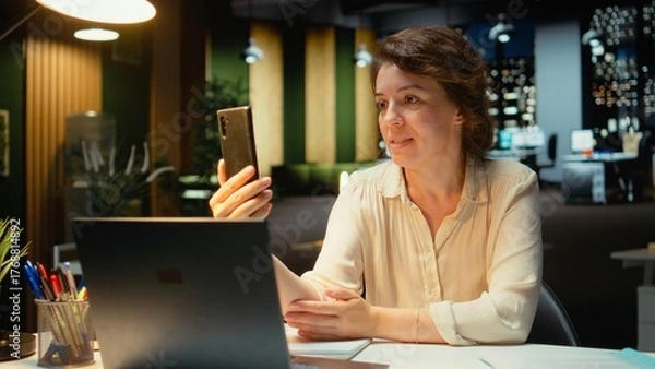 Obraz Entrepreneur joining online meeting on phone at night in office, maintaining eye contact with the webcam. Executive manager focused on communication, participating in a collaborative chat. Camera A.