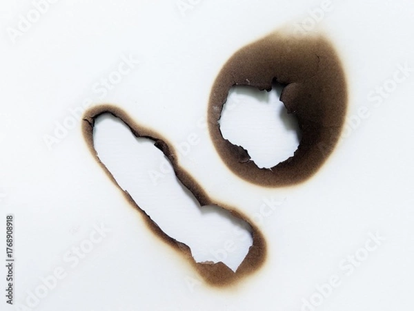 Fototapeta Close up of fire damaged hole on white paper background. Paper burn mark with black stain texture. White paper with fire burned hole.