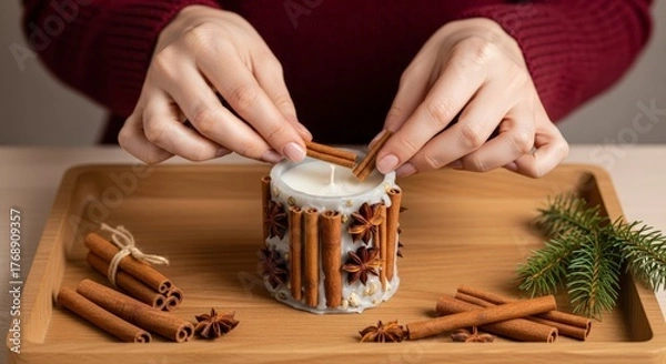 Fototapeta Hands decorating handmade candle with cinnamon sticks and dried orange for rustic holiday decor.