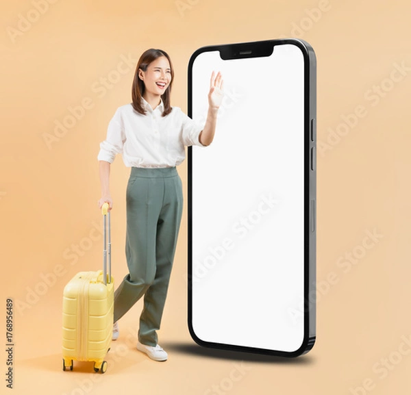 Obraz Happy Asian business woman holding suitcase and hand touching a large smartphone screen isolated on beige color background, travel concept.