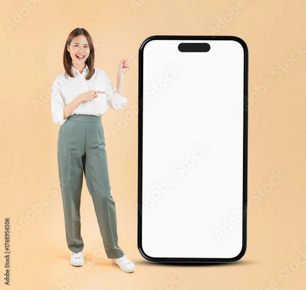 Fototapeta Happy Asian business woman hand touching a large smartphone screen isolated on beige color background, travel concept.