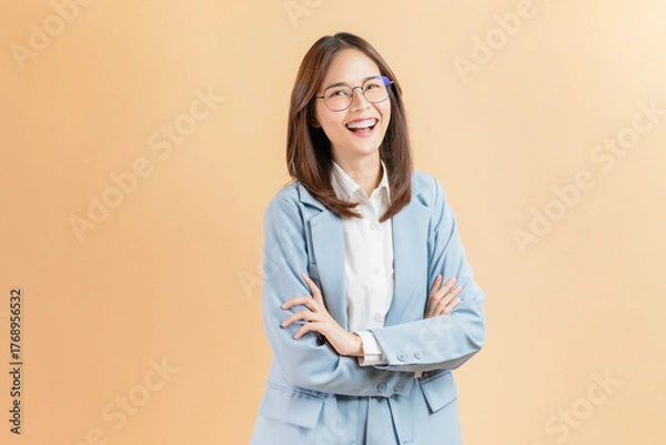 Obraz Smiling Asian businesswoman standing with arms crossed isolated against a beige background.