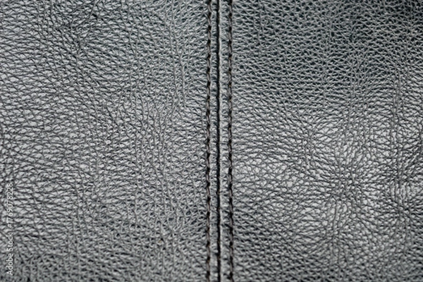 Fototapeta close-up macro of dark gray, black textured leather with a vertical stitched seam. Represents upholstery, fashion, abstract material background, and textile manufacturing detail.