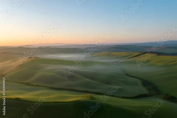 Fototapeta Golden sunrise illuminates rolling green hills and valleys shrouded in a gentle mist creating a serene and breathtaking natural landscape at dawn