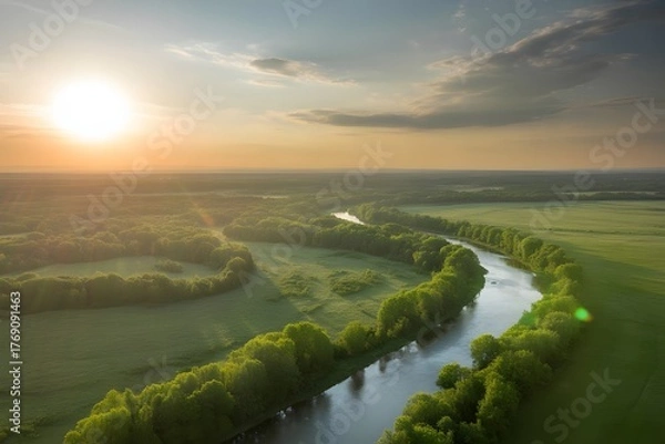 Fototapeta Golden sun setting over a winding river and lush green fields creating a serene and picturesque landscape with dramatic clouds in the sky