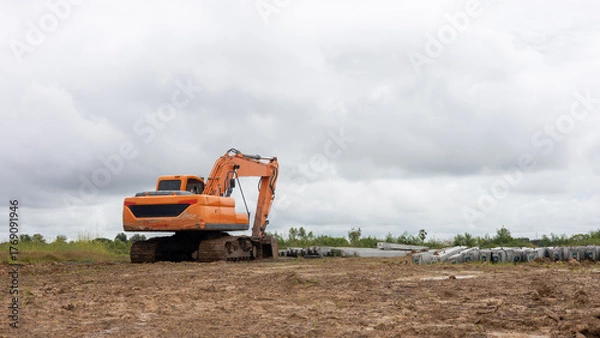 Fototapeta Low angle view of yellow backhoe on the ground near a concrete pillar.