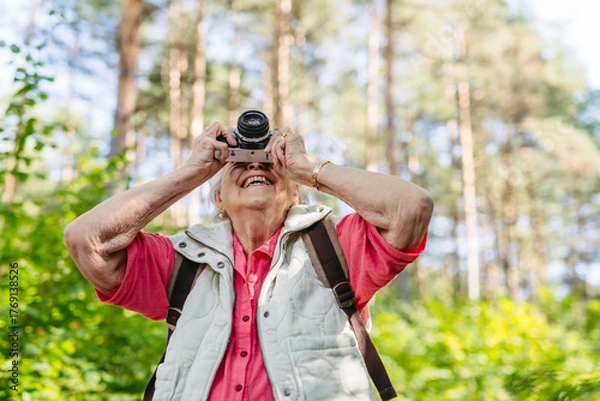 Fototapeta Elderly woman photographing nature during forest walk.