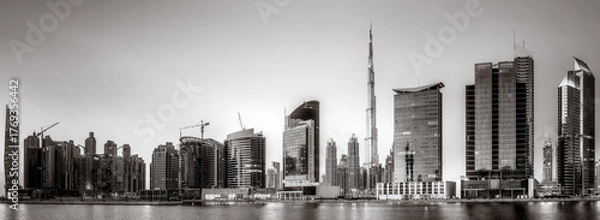 Fototapeta Monochrome city skyline with tall skyscrapers reflecting on calm water under a cloudy sky, Dubai Marina bay UAE