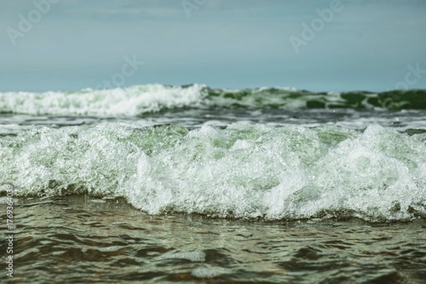 Fototapeta Small, foamy tidal waves reaching the shore, Close up, low angle, water level point of view, cloudy summer day, no people