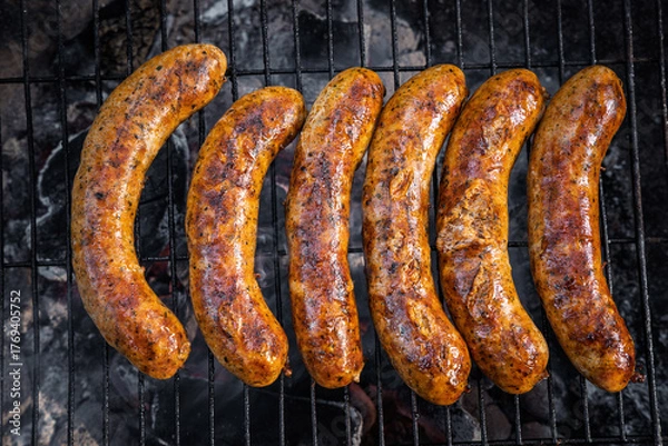 Fototapeta Rack of hot dogs are cooking on a grill. The hot dogs are brown and have a lot of seasoning on them
