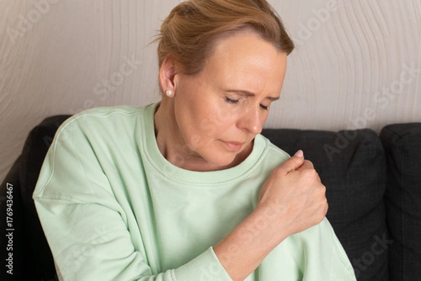 Fototapeta Close-up of woman holding shoulder in pain, suffering from joint discomfort or muscle tension. Concept of arthritis, physical health, body awareness, injury and pain relief.