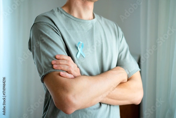 Obraz Man standing with crossed arms wearing blue satin ribbon on shirt. Concept of prostate cancer awareness in November, prevention, early diagnosis, and medical care for mens health.