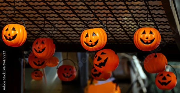 Fototapeta Orange pumpkins with scary faces decorated for Halloween hanging from a ceiling on local market