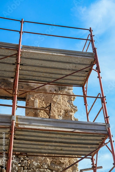 Fototapeta Metal scaffolding platforms and guardrails rise against a bright blue sky at a construction site.