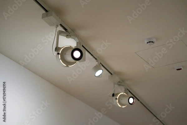Fototapeta Track lighting fixtures illuminate a modern gallery ceiling with detectors and access panel.