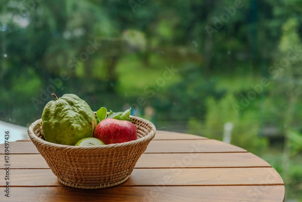 Fototapeta top view photograph of small basket of fruit included with apple orange and guava on the wood table in sunshine