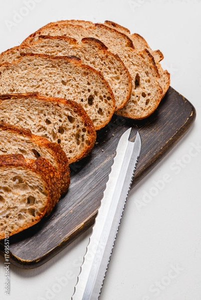 Fototapeta Close up of bread knife on wooden cutting board with sliced whole wheat sourdough bread