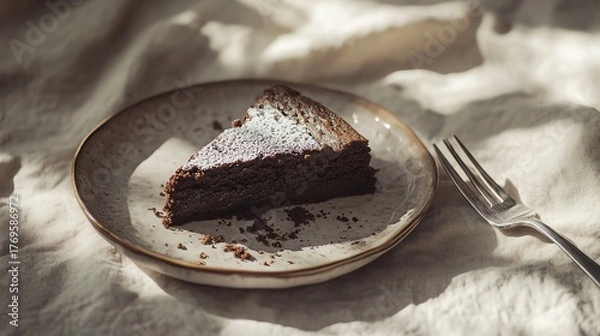 Fototapeta A halfeaten slice of chocolate cake on a handmade ceramic dish with cake crumbs and a silver fork beside it