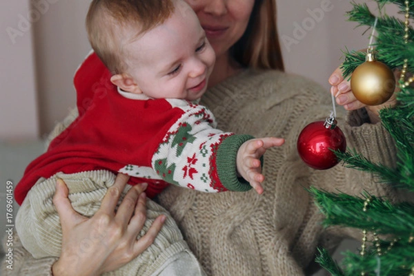 Fototapeta Mom and her newborn decorating a Christmas tree together. Copy space, background.