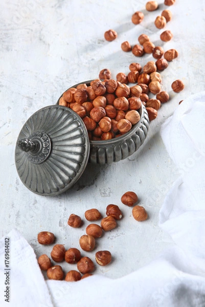 Fototapeta Hazelnuts in a tin vase. A natural product. A light background. Vertical photo.