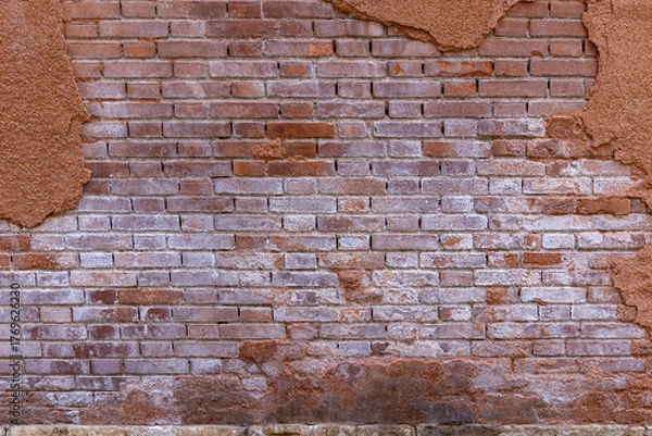 Obraz Old Weathered Brick Wall with Peeling Plaster. Close-up of an aged brick wall with partially crumbling plaster and salt stains, revealing texture and urban decay.