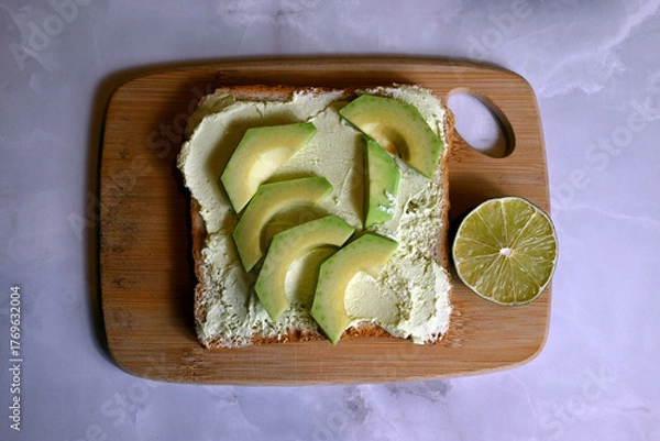 Obraz square table of bread with spread avocado butter with avocado slices on wooden board on dark background