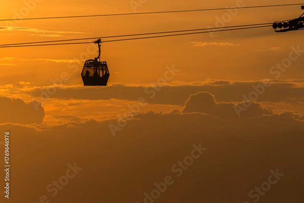 Fototapeta Cable car at sunset with the sun behind and orange-hued clouds