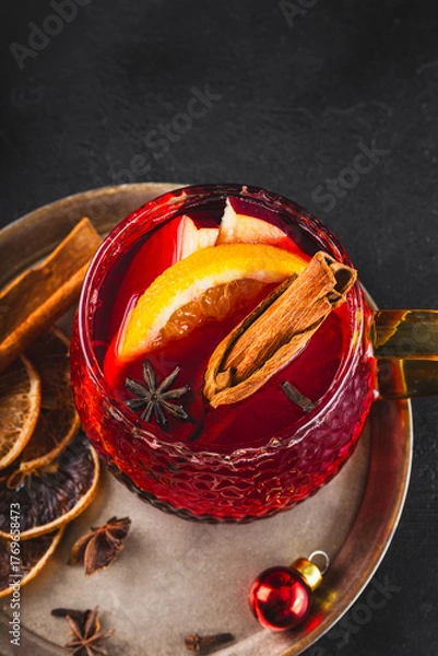 Obraz Holiday Mulled Wine with Orange and Apple in glass Mug Surrounded by Christmas Decor on black background vertical photo