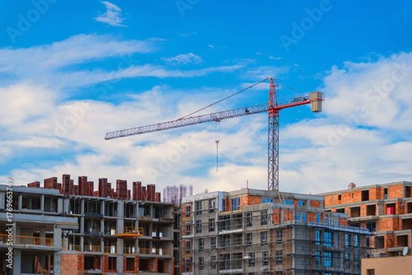 Fototapeta Construction site with modern apartment buildings under development and tower crane against blue sky. Concept of urban growth, real estate investment, infrastructure growth, residential construction