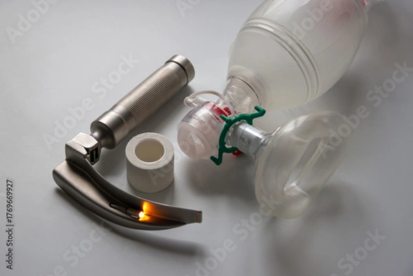 Fototapeta A laryngoscope, adhesive plaster and an Ambu breathing bag are on a white table. Horizontal shot.
