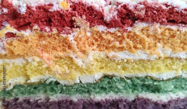 Fototapeta A cross-section of a multi-layered rainbow cake. A slice of vibrant rainbow cake with buttercream frosting. Food background.