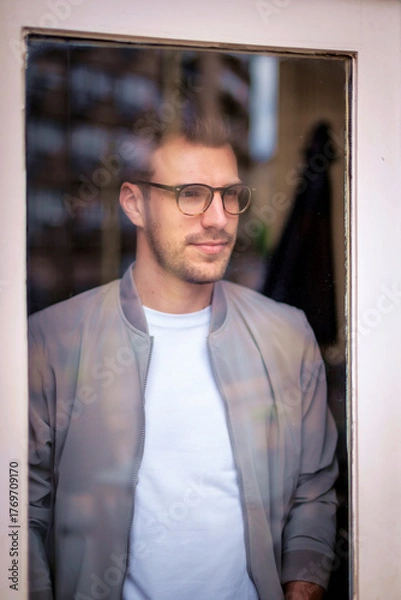 Obraz Portrait of a young man standing by the window and deep in thought