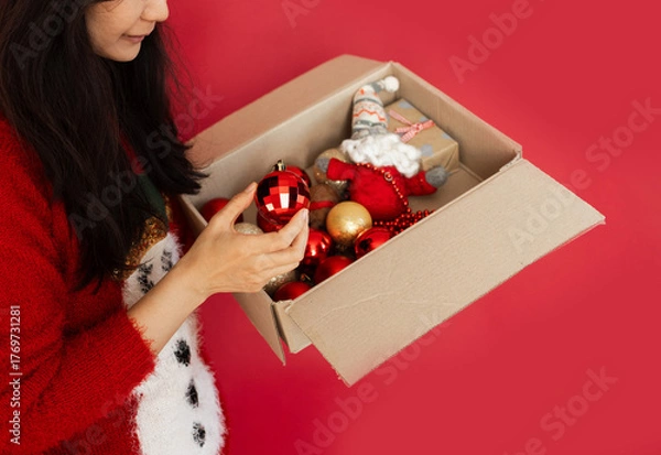 Obraz woman holding cardboard box with toys for Christmas tree ornaments. Concept of Christmas and New Year preparation. Selective focus.