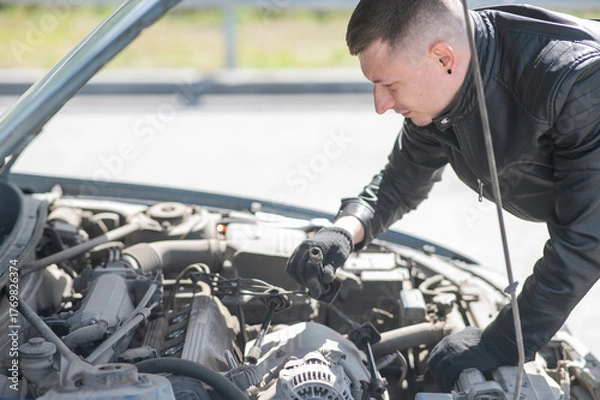 Obraz A man changes spark plugs in his car. 