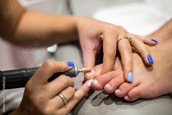 Fototapeta Master during a pedicure. The process of professional pedicures. Master in mask making pedicure under the lamp. The concept of beauty and health. Vertical photo.
