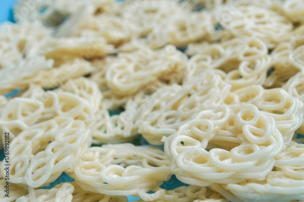 Fototapeta Close-up with selective focus on raw, uncooked Indonesian crackers (Krupuk) in a spiral, ring shape. Represents Asian snack food, abstract texture, culinary detail, and food preparation background.