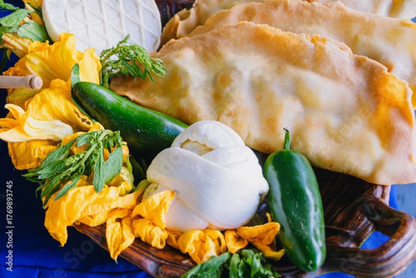 Fototapeta Molotes (fried Mexican street food) served with fresh cheese, squash blossoms, and jalapeño chiles on a rustic plate.