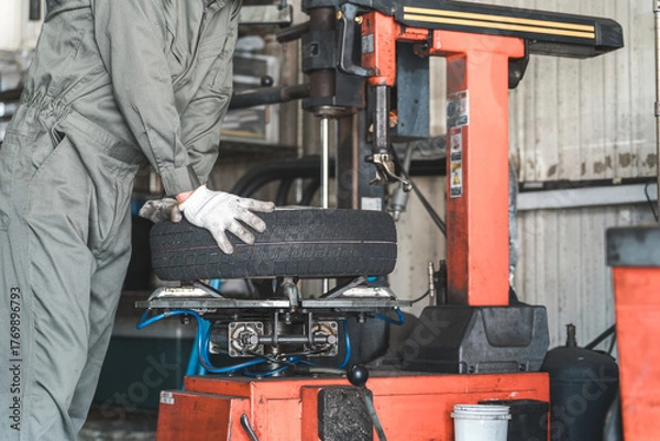 Fototapeta タイヤチェンジャーを使いタイヤの組み替えをするメカニック・整備士の男性作業員
