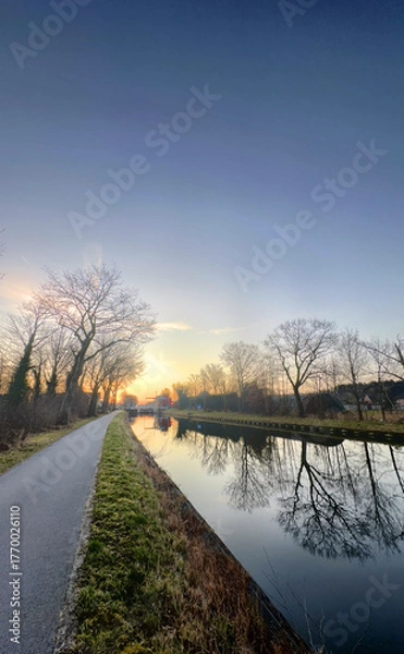 Fototapeta A tranquil and peaceful canal scene unfolds at sunset, showcasing trees and their reflections in the still water